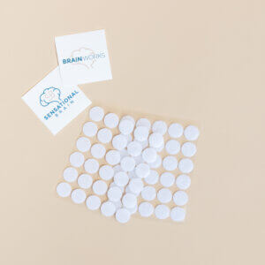 Sheet of white Velcro coins on beige surface with two logo cards nearby.