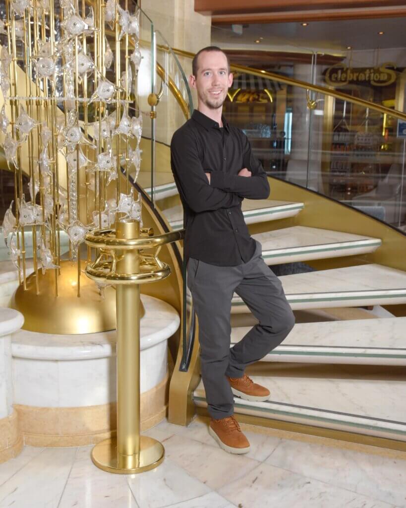 A person in a black shirt and gray pants stands by a golden staircase, suitable for BrainWorks discussions.