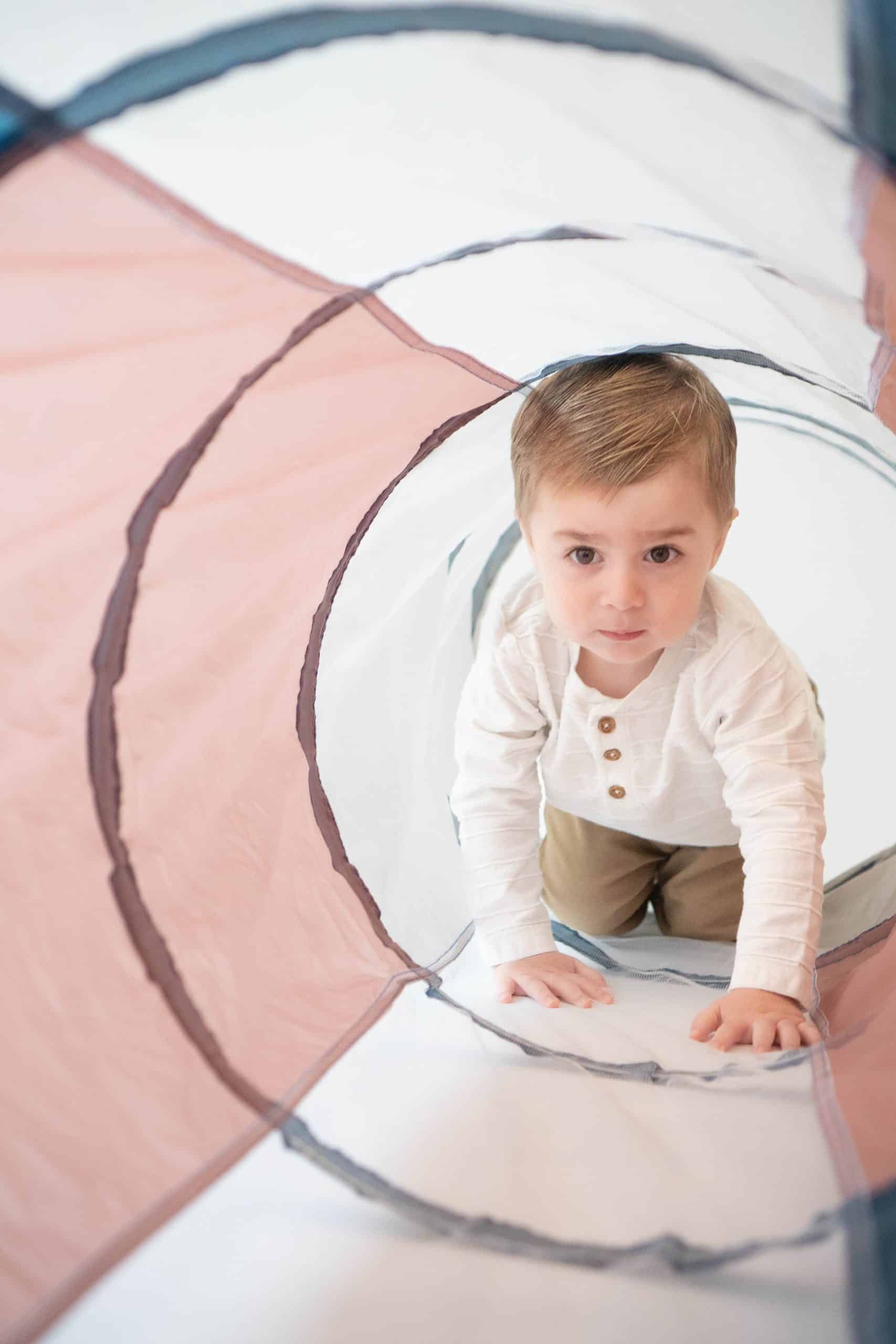 Child crawling through a colorful play tunnel, enjoying exploration in the Sensational Brain Crawling Tunnel.